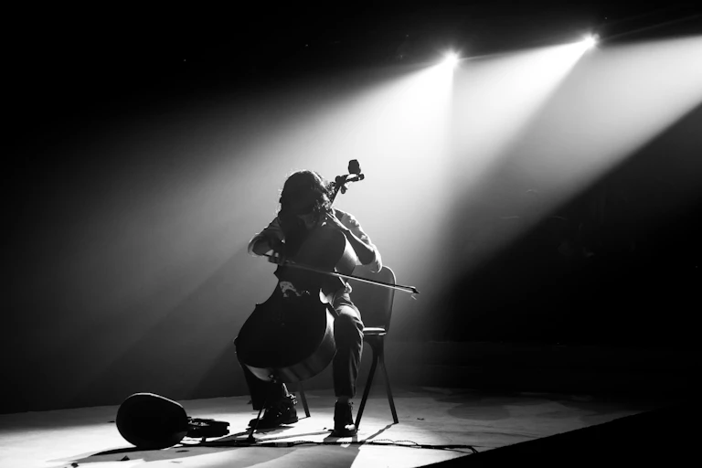 A cello player alone on stage, silhouetted by spotlights.