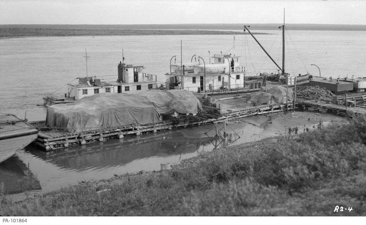 A vintage black-and-white photograph of a wharf with two shipping vessels docked.