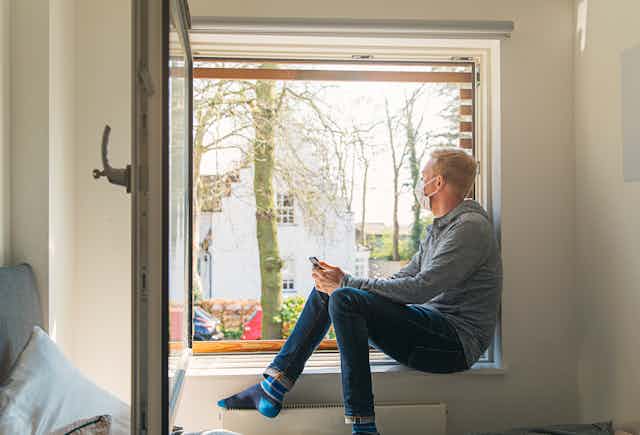 A man with a mask on sitting in a large open window.