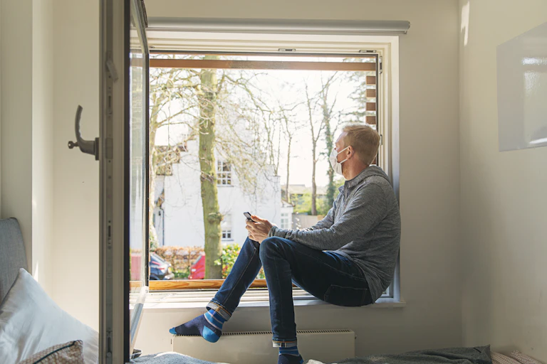 A man with a mask on sitting in a large open window.