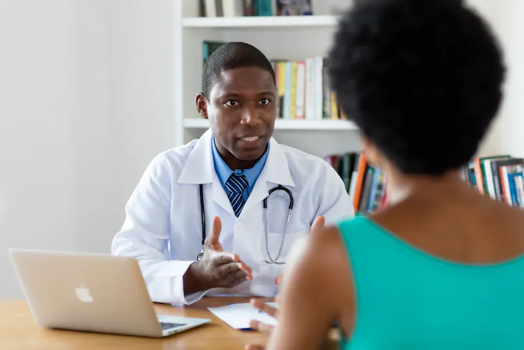 A doctor is seated at a table talking to a patient.