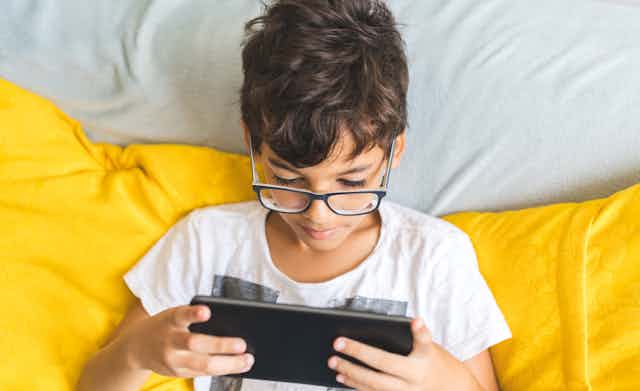 Boy uses a digital tablet on a yellow sofa.