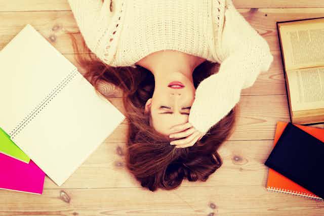 Girl lying on her back with her hand on her forehead, books lying open around her