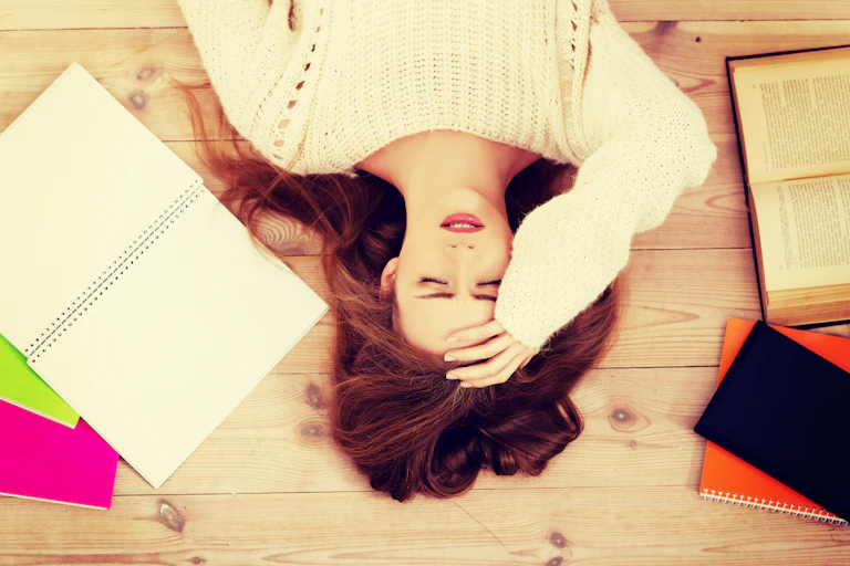 Girl lying on her back with her hand on her forehead, books lying open around her