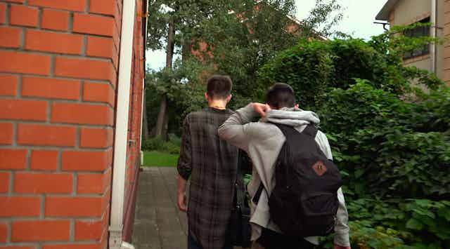 Two boys walk along side of house