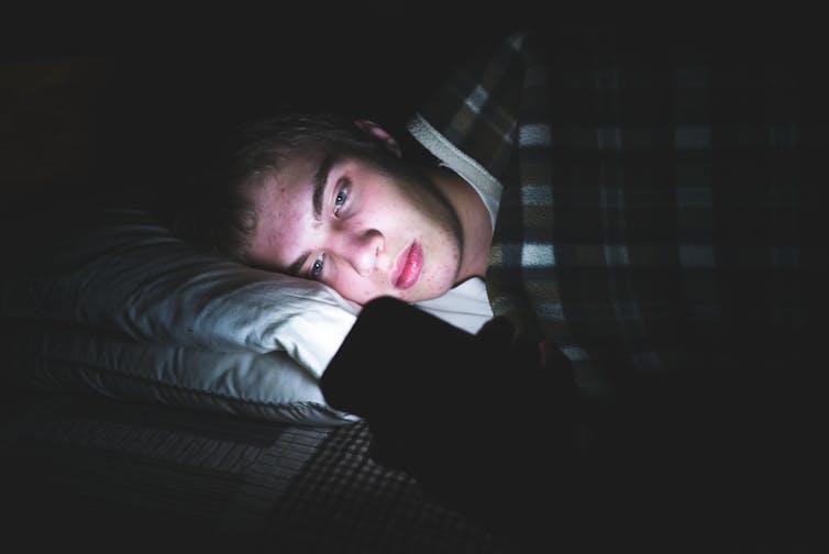 A young man looks at his phone in bed.
