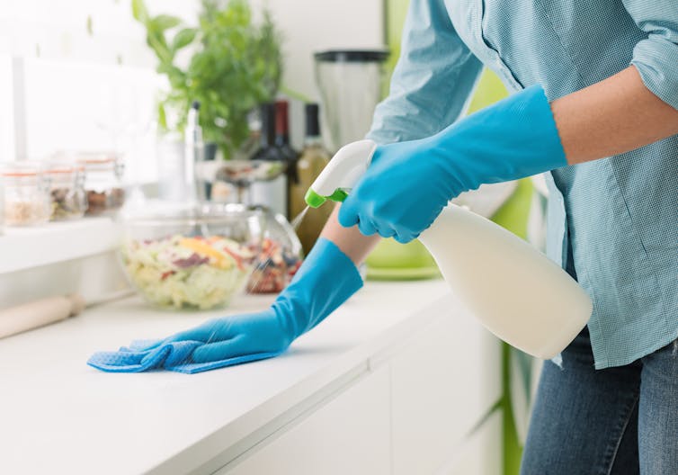 Gloved hands wiping kitchen bench.