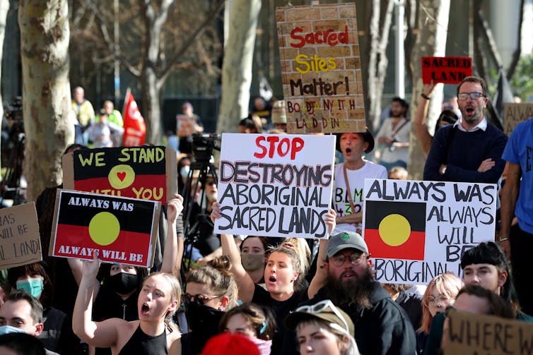A group of protesters holding signs that read 'stop destroying Aboriginal sacred lands'.
