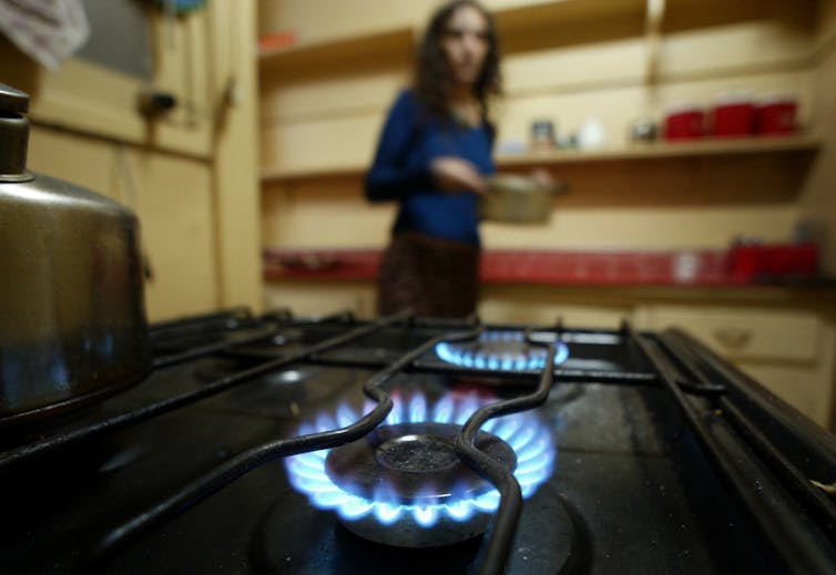 A woman stands in front of a gas burner.