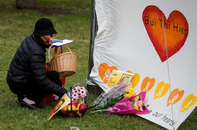 A woman wearning a mask lays flowers at makeshift memorial for a dead Cargill worker.