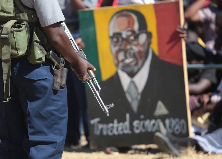 Armed guard in front of a Robert Mugabe poster.