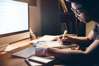 Um jovem senta-se em frente a uma tela de computador destacando notas