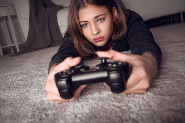 Teenage girl lying on floor playing games console.