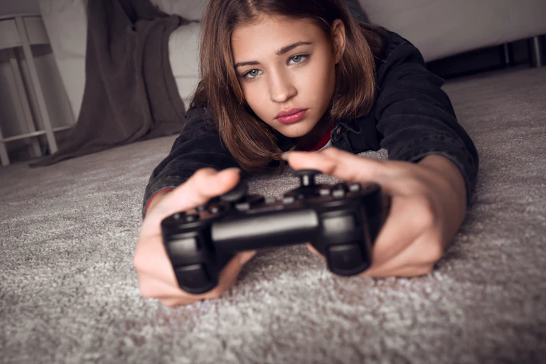 Teenage girl lying on floor playing games console.
