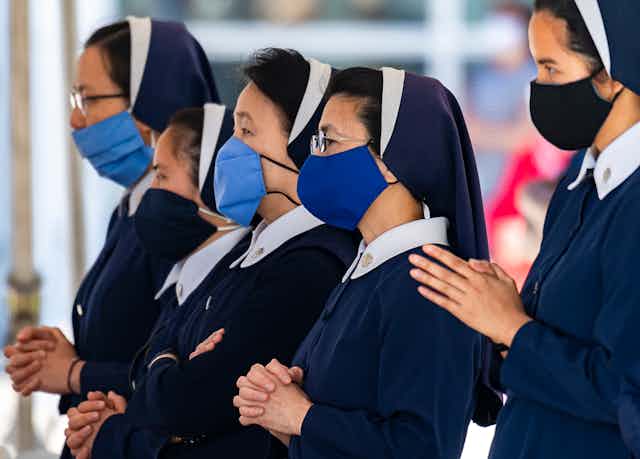 Four nuns wearing masks during a church service