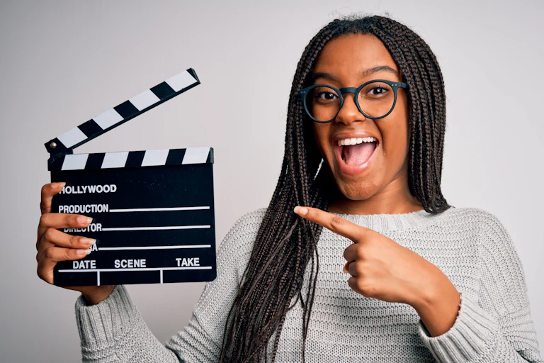 Woman points to a clapperboard she's holding up.