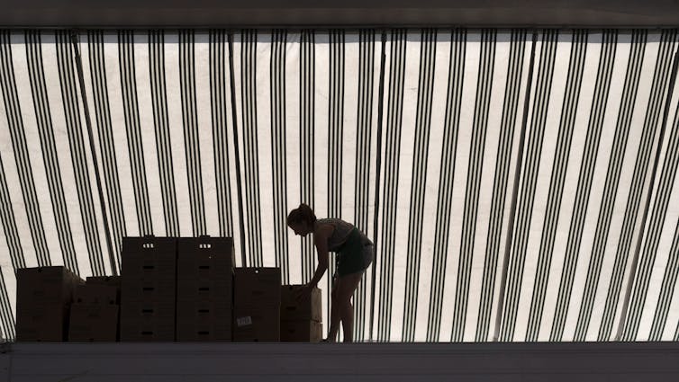 A woman bends to arrange boxes in a kiosk at a farmer's market.