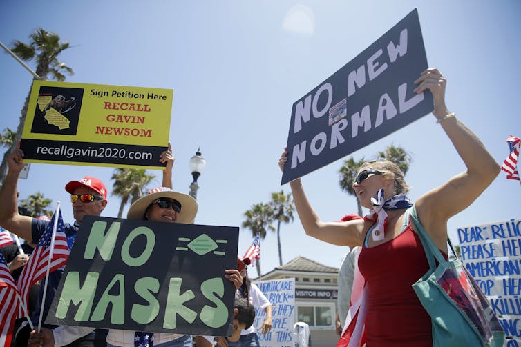 Protesters hold signs that read No Masks and No New Normal at a protest in the California sunshine.