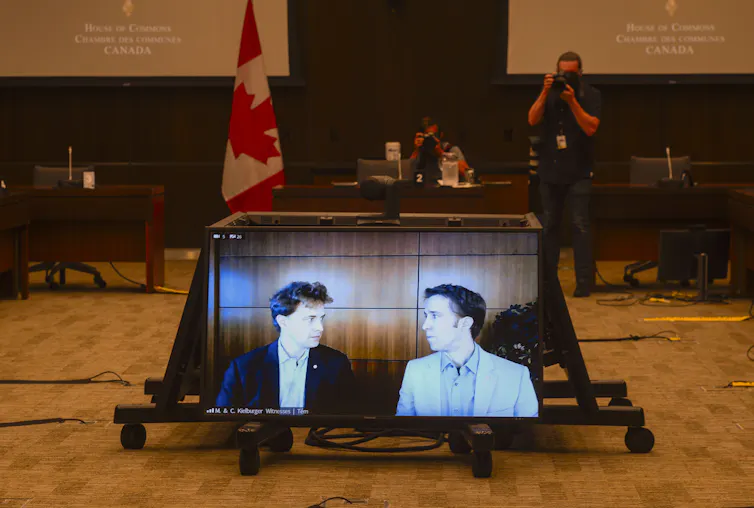 Marc Kielburger and Craig Kielburger appear on a screen in a government building.