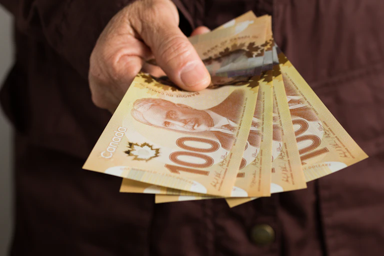A hand holds a wad of Canadian $100 bills.