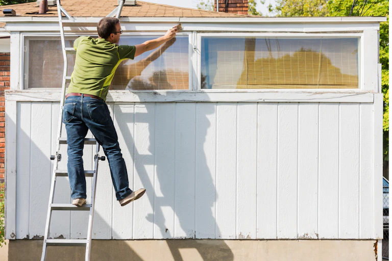 Man painting shed standing precariously on ladder.
