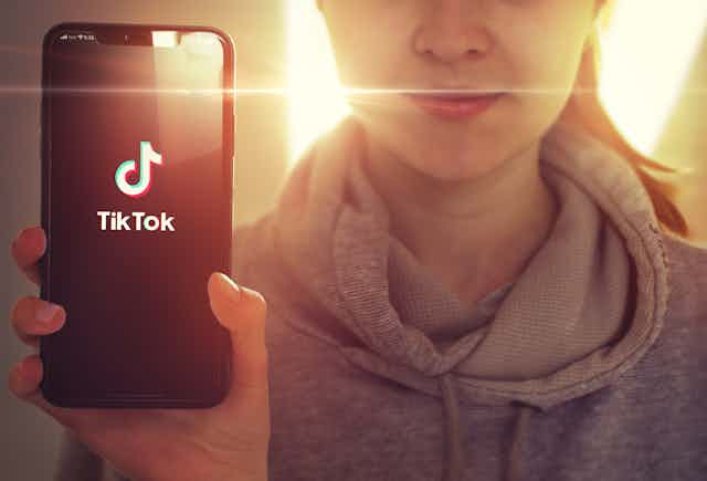 A young girl holding up a smartphone with the TikTox app showing.