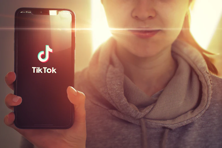 A young girl holding up a smartphone with the TikTox app showing.