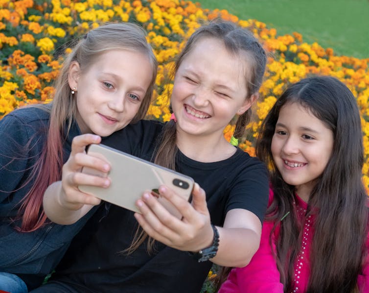 Three young girls video themselves on a smartphone.