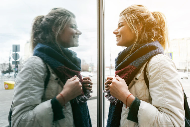 A woman looking at her reflection in the window of a building.
