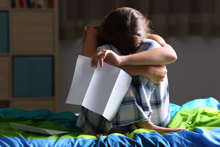 Dejected girl sitting on bed head in hands with exam results letter