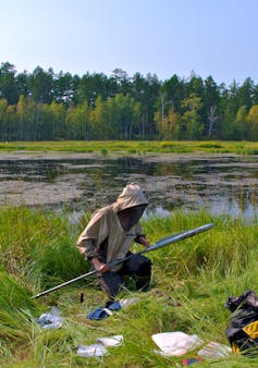 Scientist in protective clothing sat beside lake in peat bog