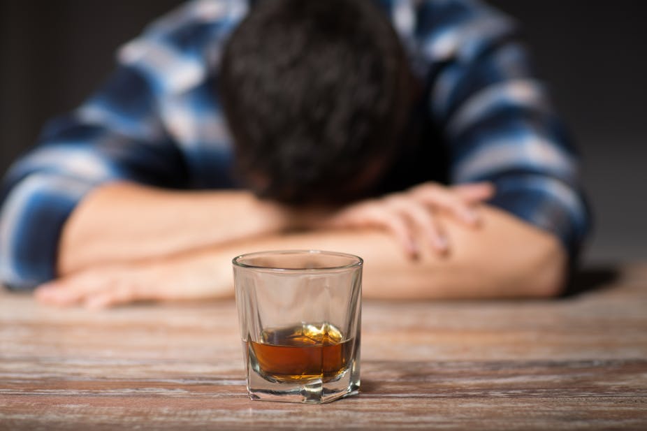 Man slumped over on table with half-full glass in front of him.