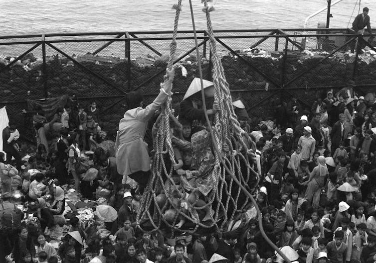 A cargo net lifting Vietnamese refugees from a barge onto a larger U.S. ship