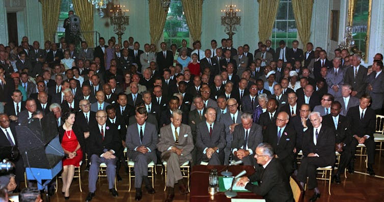 President Johnson enacting the Civil Rights Act of 1964 before a large audience.