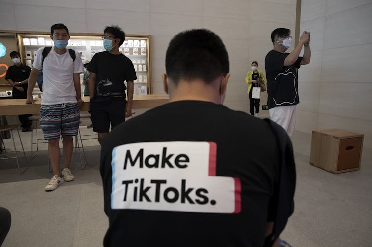 A photograph of a man's back wearing a shirt promoting TikTok in an Apple Store