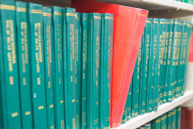 A row of green hardbound journals, with one with a red cover sticking out