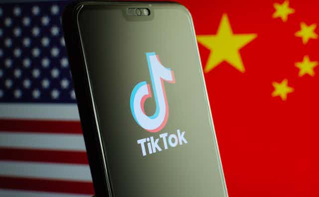 A composite image of the American and Chinese flags separated by a mobile phone displaying the TikTok logo.