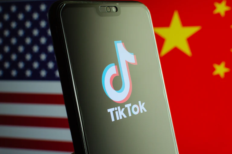 A composite image of the American and Chinese flags separated by a mobile phone displaying the TikTok logo.