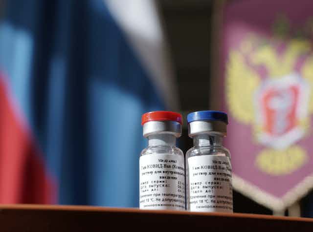 two vials of vaccine in front of Russian flag