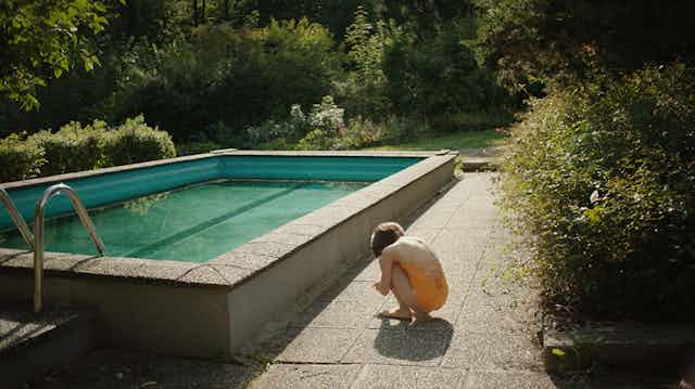 Movie still of a pool and the back of young girl in a yellow bathing suit