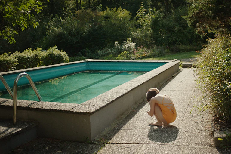 Movie still of a pool and the back of young girl in a yellow bathing suit