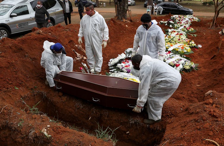 Gravediggers in protective suits lower a coffin into place alongside the graves of other coronavirus victims in Sao Paulo, Brazil