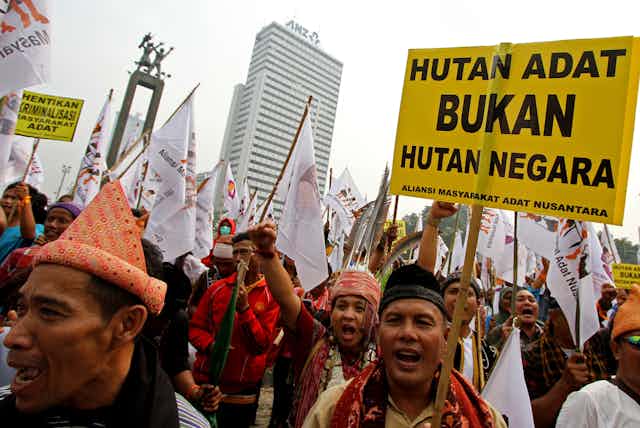 Dozens of men wearing traditional outfits holding protest signs. 