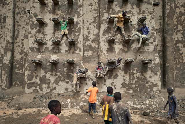 Children climb on the walls of a large mud brick structure as new mud is applied to it.