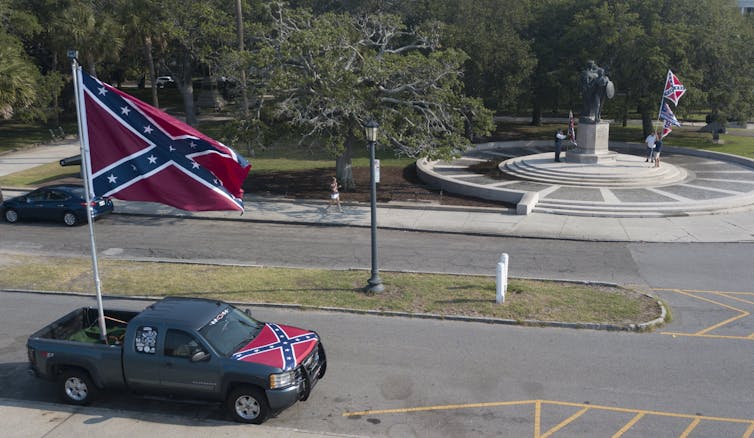 A truck carrying a Confederate battle flag is parked next to a Confederate statue.
