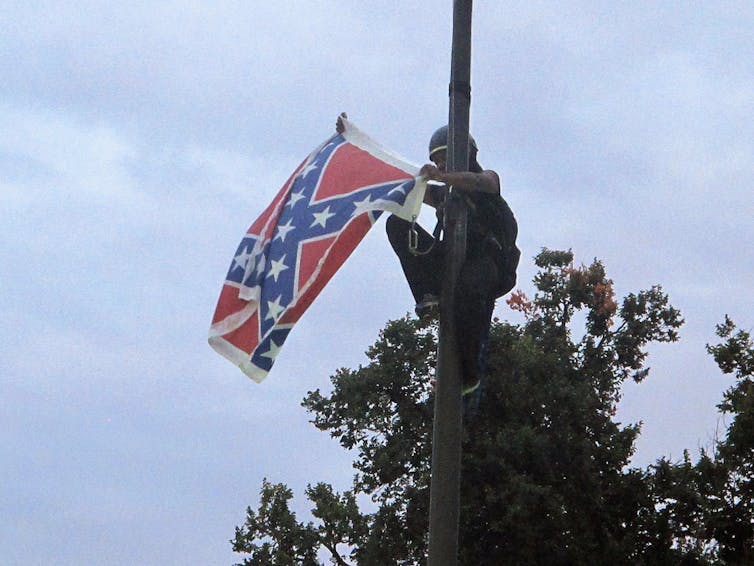 A woman takes a Confederate flag off a public display.