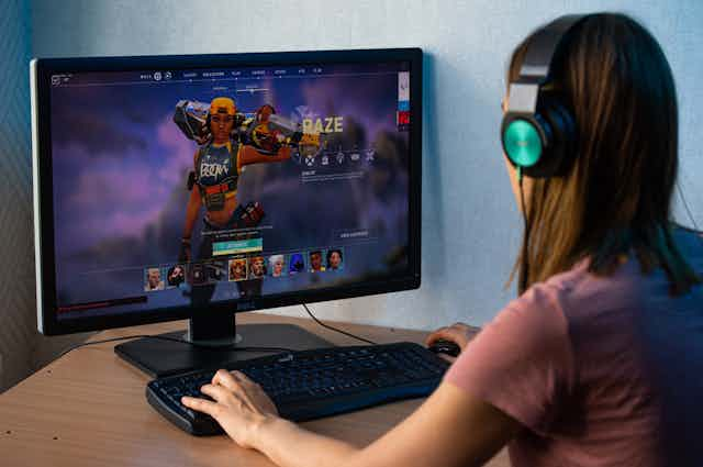 A young woman sits in front of a computer screen showing the video game Raze