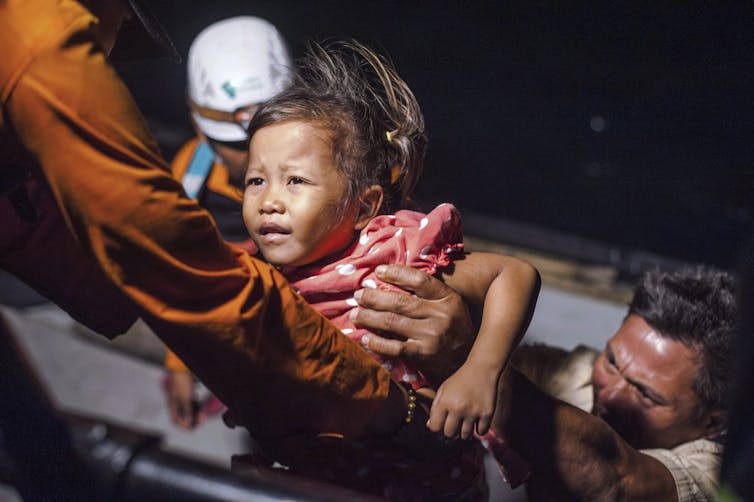 A girl is passed from a boat into the arms of a rescuer