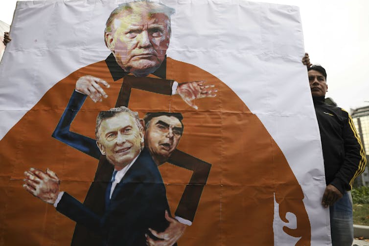 A man holds a banner with the images of Trump, Bolsonaro and Argentina's President Mauricio Macri making a swastika.