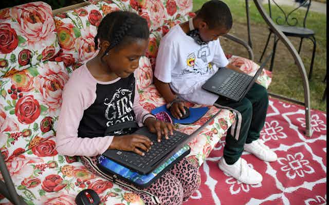 Fourth-grader Sammiayah Thompson, left, and her brother third-grader Nehemiah Thompson work outside in their yard on laptops provided by their school system for distant learning in Hartford, Connecticut.